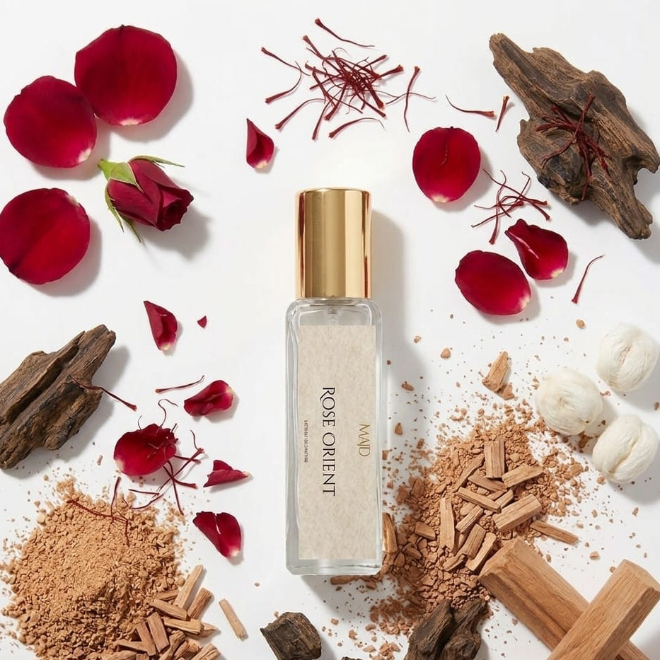 Rose Orient perfume bottle surrounded by rose petals, saffron, and wood pieces on a white background